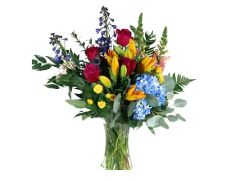 A mixed floral bouquet containing red roses, yellow lilies, blue hydrangeas, and greenery arranged in a clear glass vase.