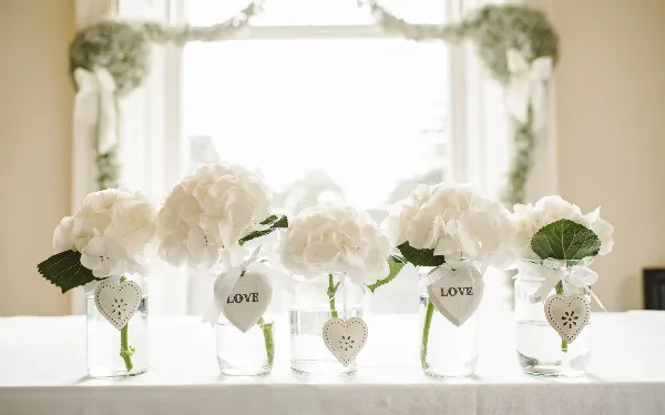 A wedding table setting with white linens and white floral centerpieces in glass vases.