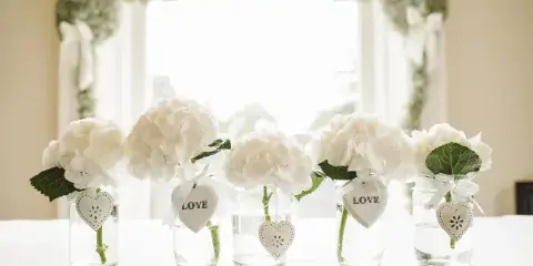 A wedding table setting with white linens and white floral centerpieces in glass vases.