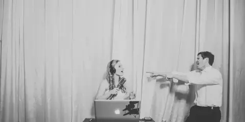 A DJ performing at an event with a laptop and microphone, interacting with a guest.