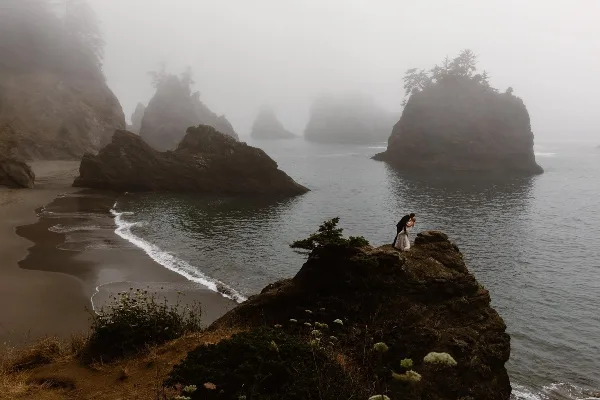 A wedding couple embracing on a rocky outcrop overlooking a misty, dramatic coastline.