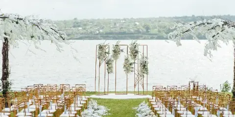 Outdoor wedding ceremony setup with a floral arch, gold chairs, and white floral aisle decorations.