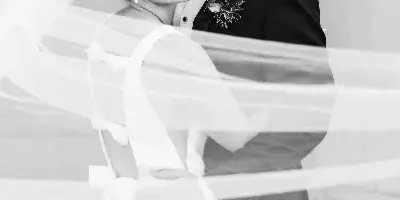A black and white portrait of a bride and groom sharing a tender moment, with the bride's veil flowing in the foreground.