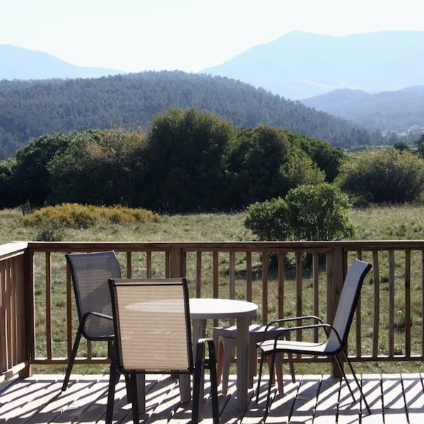 A wooden deck with a table and chairs overlooking a scenic mountain landscape.