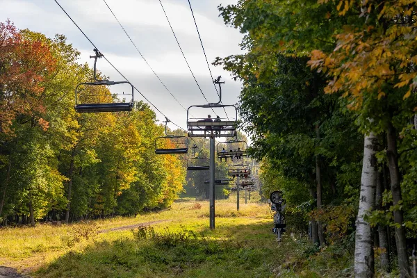 A chairlift carrying passengers up a wooded slope with autumn foliage.