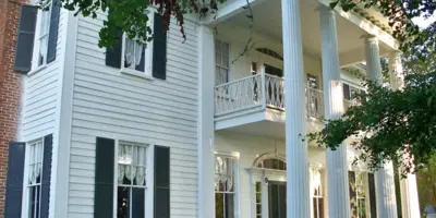 Exterior view of a historic white two-story home with a large porch and columns.