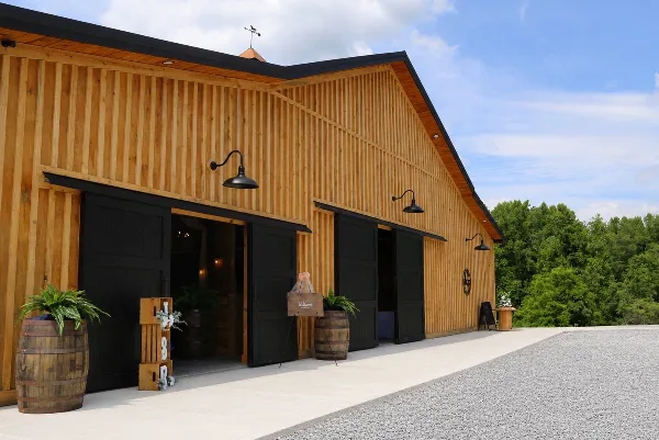 Exterior view of a wooden barn wedding venue with black doors and a gravel driveway.