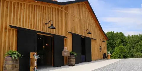 Exterior view of a wooden barn wedding venue with black doors and a gravel driveway.