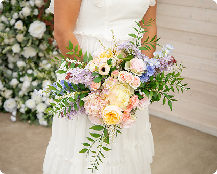 A close-up of a colorful bridal bouquet held by a bride in a white dress.