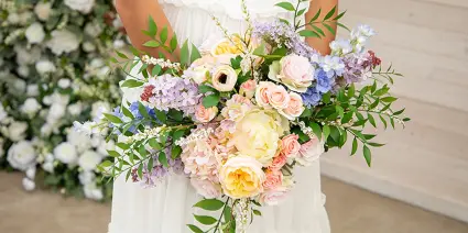 A close-up of a colorful bridal bouquet held by a bride in a white dress.