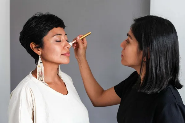 A makeup artist applying makeup to a client's face with a brush.