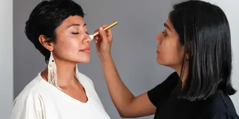 A makeup artist applying makeup to a client's face with a brush.