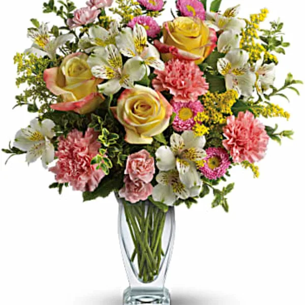 Mixed bouquet of roses, alstroemeria, carnations, and yellow filler flowers in a clear glass vase