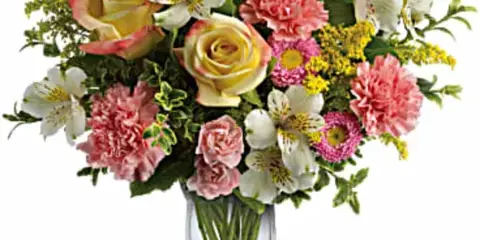 Mixed bouquet of roses, alstroemeria, carnations, and yellow filler flowers in a clear glass vase