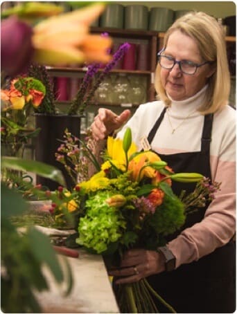 A florist wearing an apron arranging a colorful bouquet of flowers in a shop.