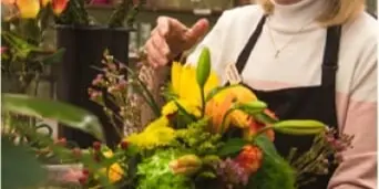 A florist wearing an apron arranging a colorful bouquet of flowers in a shop.
