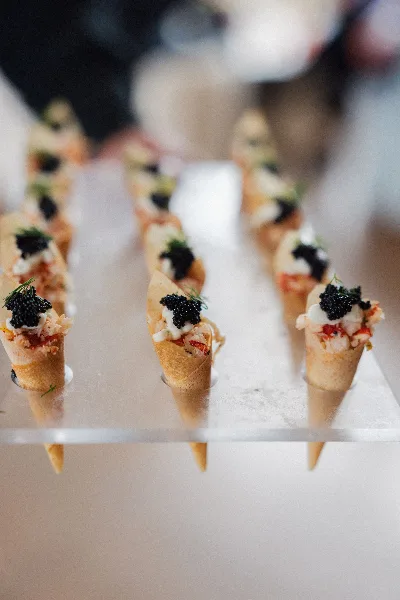A row of gourmet canapés topped with caviar and herbs arranged on a clear acrylic serving stand.
