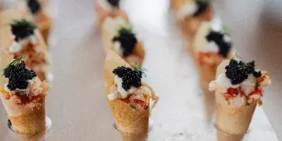 A row of gourmet canapés topped with caviar and herbs arranged on a clear acrylic serving stand.