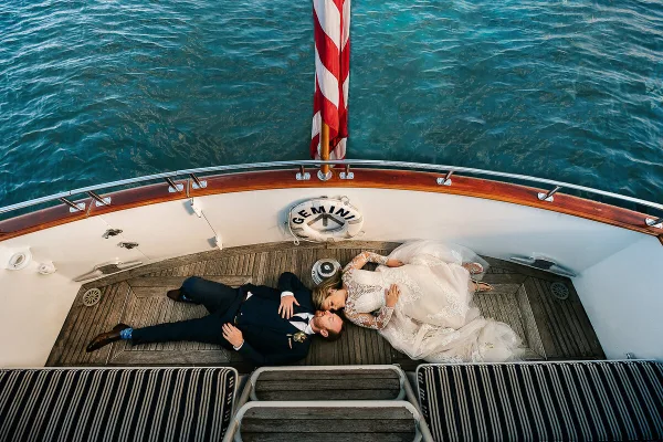 A bride and groom lying on the deck of a boat, viewed from above, with the ocean in the background.