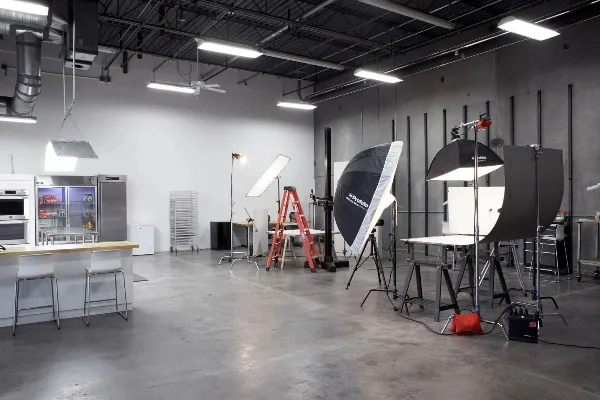 Interior of a professional photography studio featuring lighting equipment, backdrops, and a kitchen area.