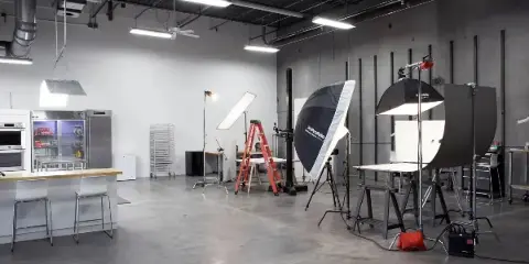 Interior of a professional photography studio featuring lighting equipment, backdrops, and a kitchen area.