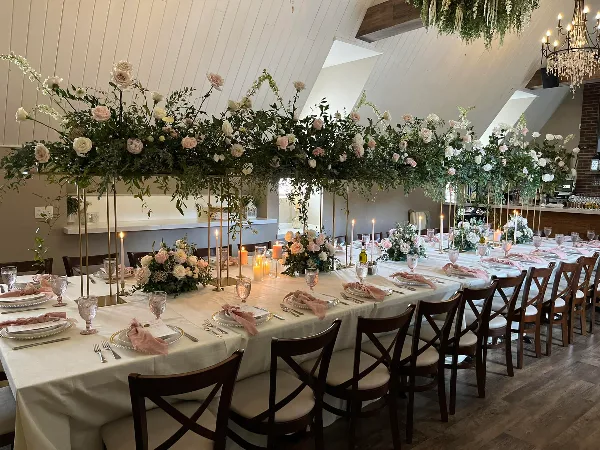A long banquet table set for a wedding with white linens, floral centerpieces, and candles.