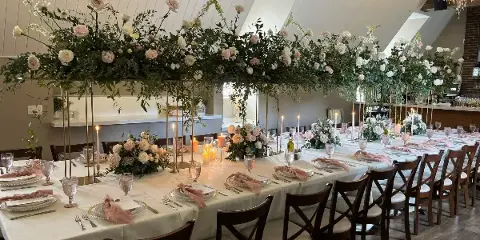 A long banquet table set for a wedding with white linens, floral centerpieces, and candles.