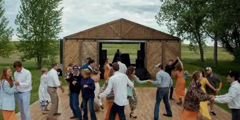 Guests dancing on a wooden floor in front of a mobile wooden barn venue in a grassy field.