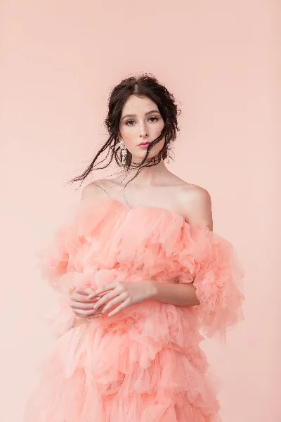A woman with styled hair and professional makeup wearing a pink ruffled dress.