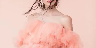 A woman with styled hair and professional makeup wearing a pink ruffled dress.