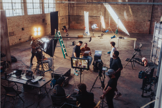 A film crew operating cameras and lighting equipment in a large studio space.