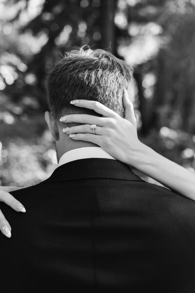 Black and white photo of a bride's hand with a ring resting on a groom's shoulder.
