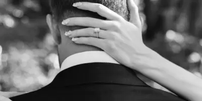 Black and white photo of a bride's hand with a ring resting on a groom's shoulder.