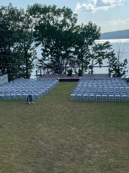 Outdoor wedding ceremony setup with white chairs and a wooden deck overlooking a lake.