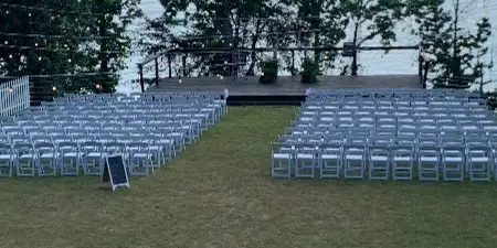 Outdoor wedding ceremony setup with white chairs and a wooden deck overlooking a lake.
