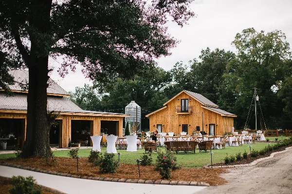 Outdoor view of a rustic wooden barn wedding venue with a grassy lawn, reception tables, and a silo in the background.