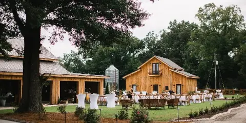 Outdoor view of a rustic wooden barn wedding venue with a grassy lawn, reception tables, and a silo in the background.