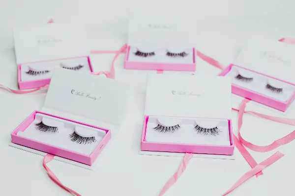 Several open boxes containing pairs of false eyelashes arranged on a white surface with pink ribbons.