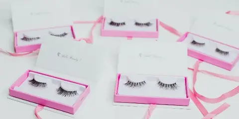 Several open boxes containing pairs of false eyelashes arranged on a white surface with pink ribbons.