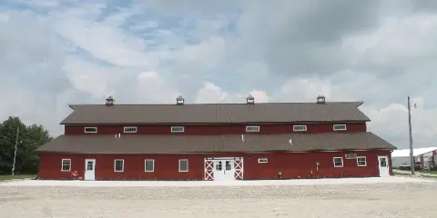 Exterior view of a large red barn event venue with a brown metal roof and white doors.