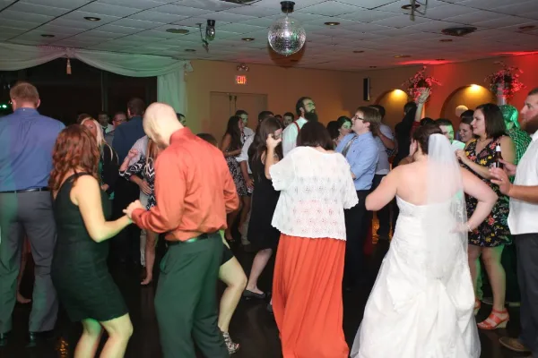 A bride and guests dancing at a wedding reception under a disco ball and colored lights.