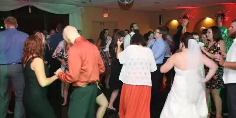 A bride and guests dancing at a wedding reception under a disco ball and colored lights.
