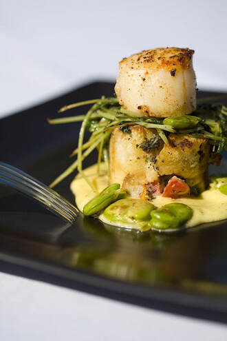 A close-up of a plated dish featuring a seared scallop atop a vegetable base with green beans and sauce.