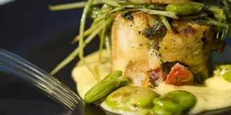 A close-up of a plated dish featuring a seared scallop atop a vegetable base with green beans and sauce.
