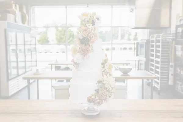 A white, four-tiered wedding cake decorated with cascading pastel flowers on a stand.
