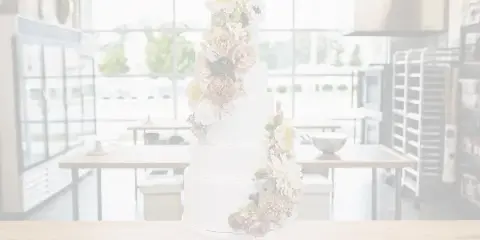 A white, four-tiered wedding cake decorated with cascading pastel flowers on a stand.