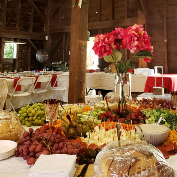 A catering buffet table filled with appetizers, cheese, fruit, and bread in a rustic venue.