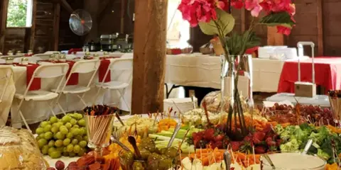 A catering buffet table filled with appetizers, cheese, fruit, and bread in a rustic venue.