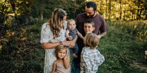 A family of five posing together in a grassy field with a forest background.