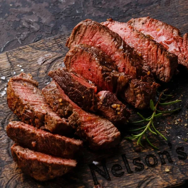 Sliced grilled steak served on a wooden board branded with the name Nelson's